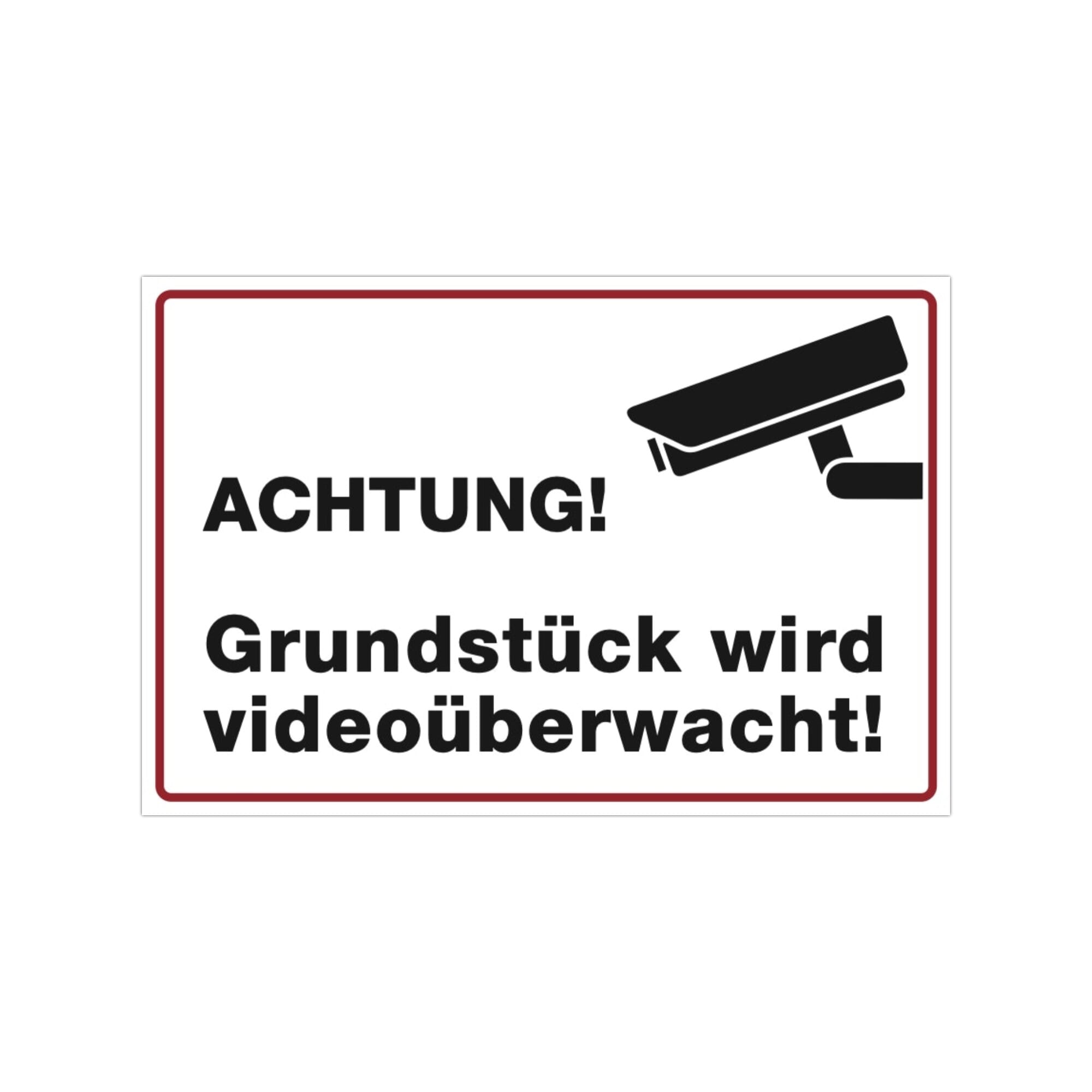 Drei weiße Aufkleber mit "Achtung! Grundstück wird videoüberwacht" in 300x200 mm, auf einer Oberfläche sichtbar